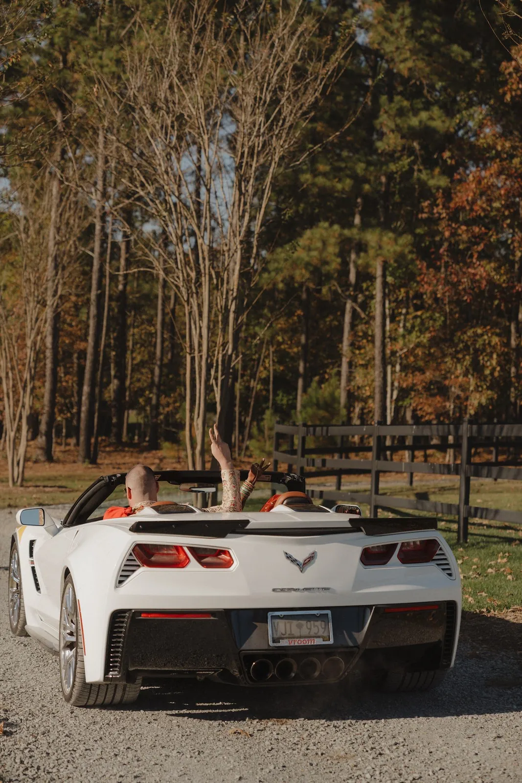 Newlyweds waving from a white convertible as they drive off through the pines