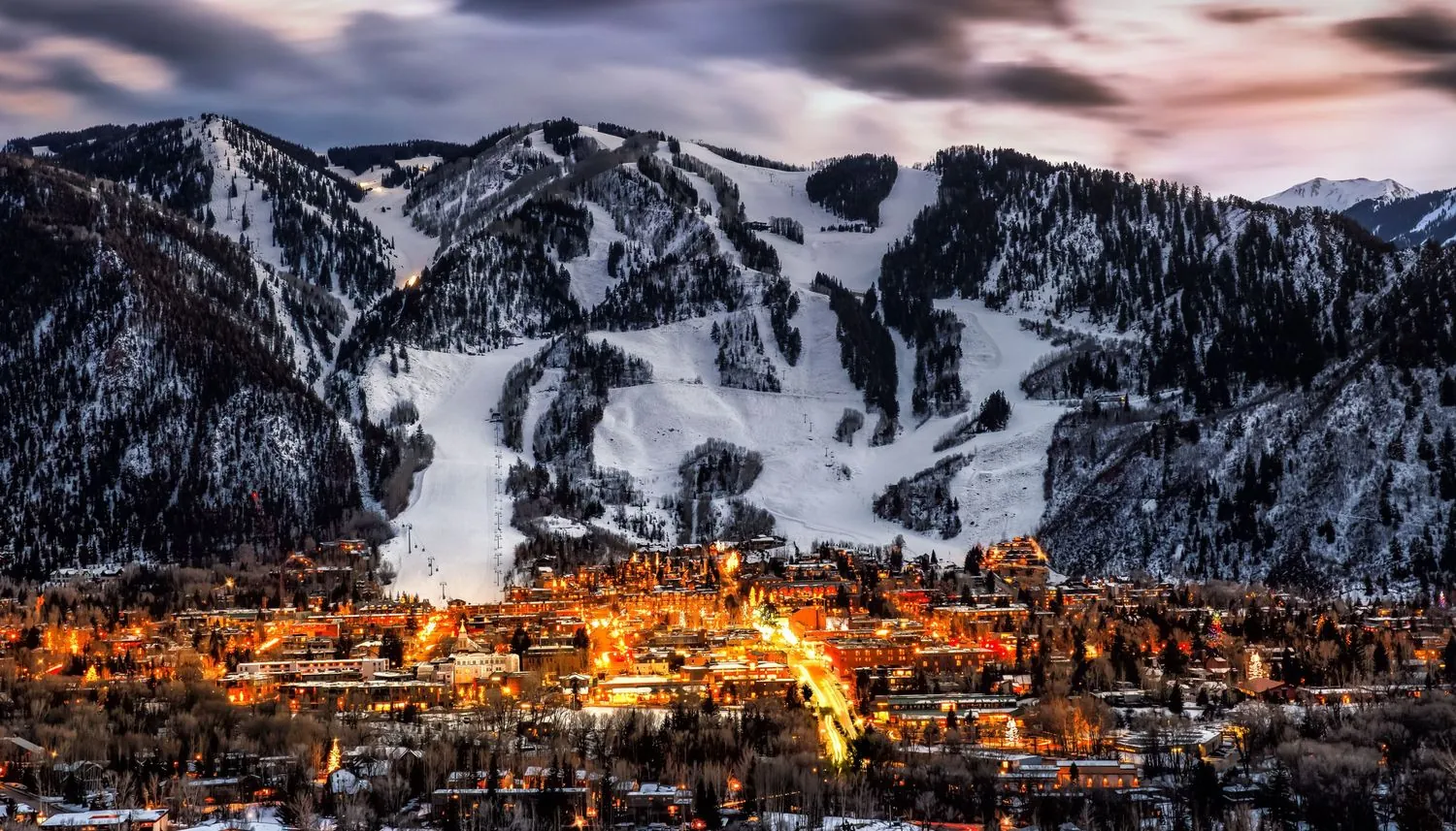 Snow-covered ski mountain rising above a Colorado town lit up at dusk