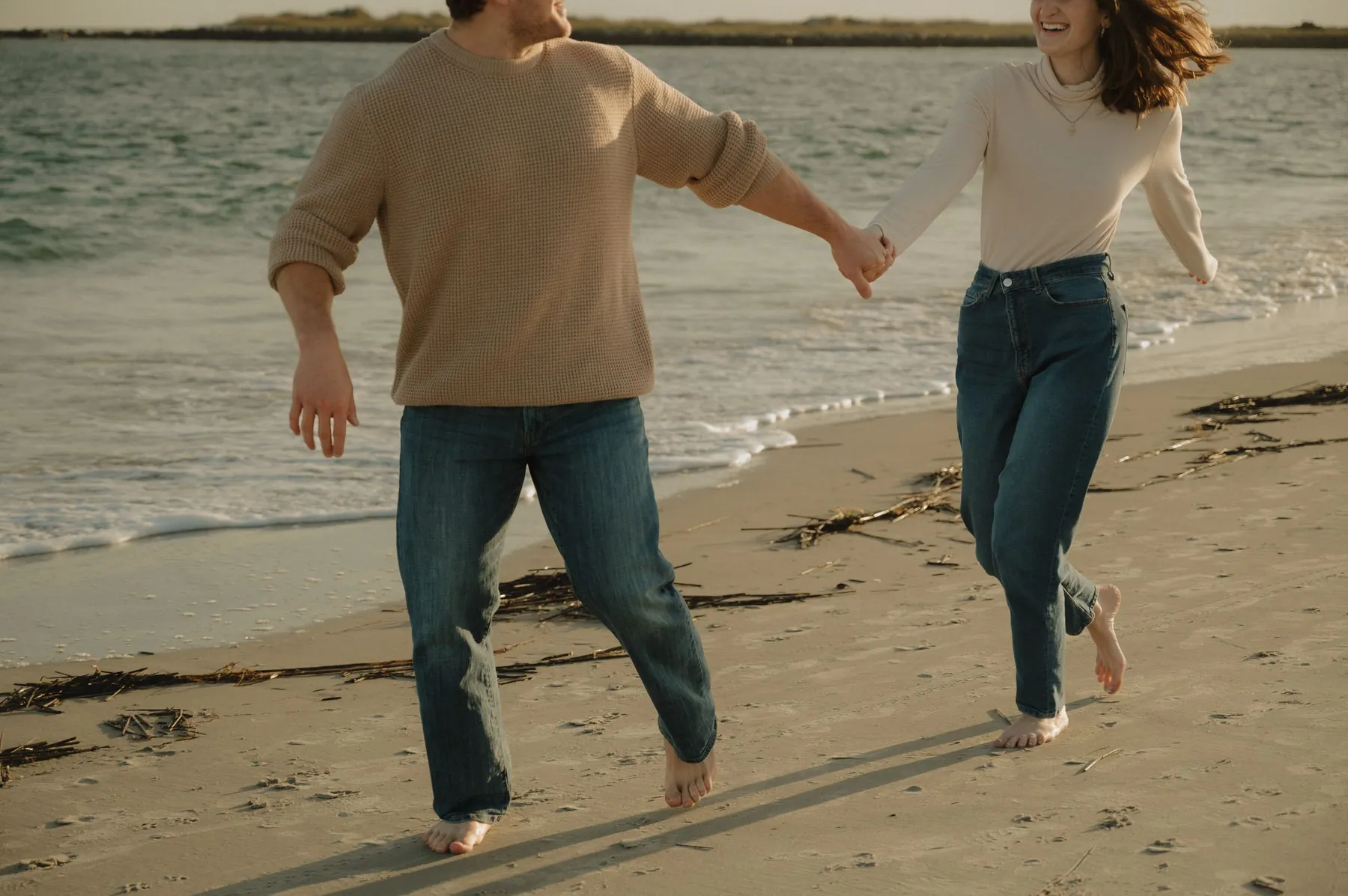 Engaged couple running hand in hand along the water at sunset