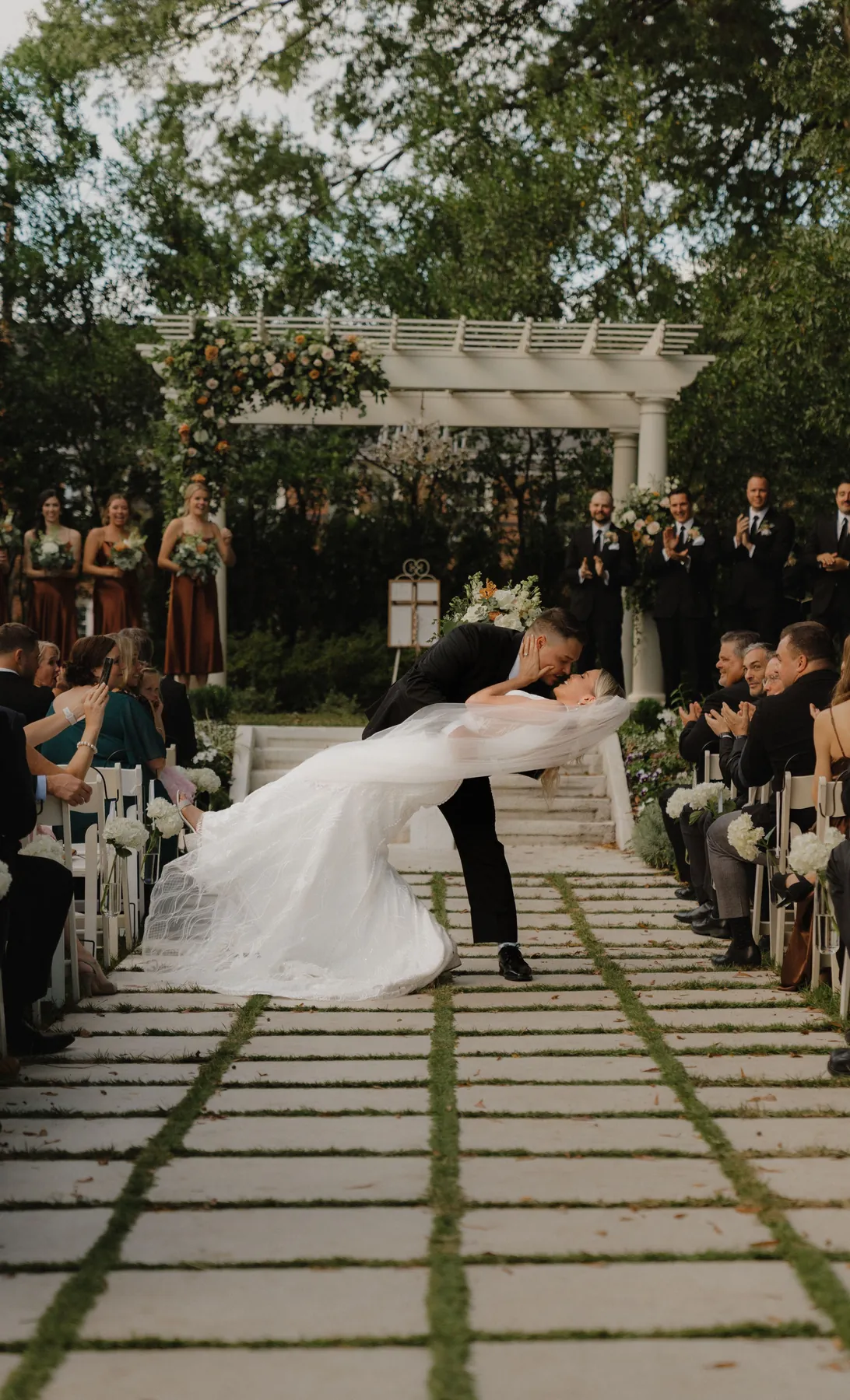 Groom dipping his bride for a kiss in the aisle after their garden ceremony